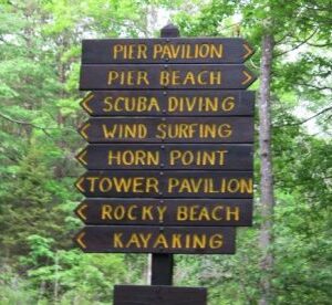 a sign brown sign with yellow lettering pointing in different directions in a park
