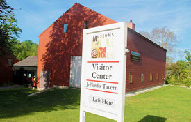 exterior image of a museum visitor center sign outside of a big red museum barn