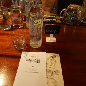 a glass, a bottle and a name tag that reads "Judy" along with a personalized pamphlet for a cocktail class