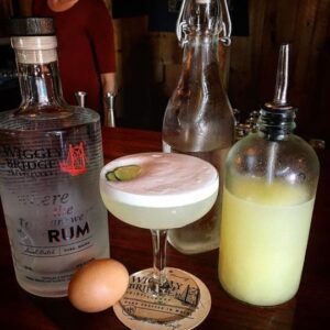a bottle of rum on a table with a yellow cocktail with a lime garnish and an egg