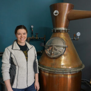 a woman with her hair pulled back and a zip up sweatshirt at a distillery