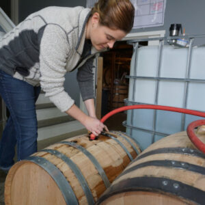a woman leaning over a barrel inserting a red tube into it