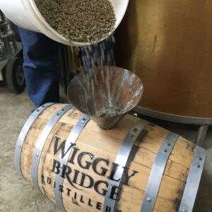 someone pouring coffee beans into a wiggly bridge distillery barrel